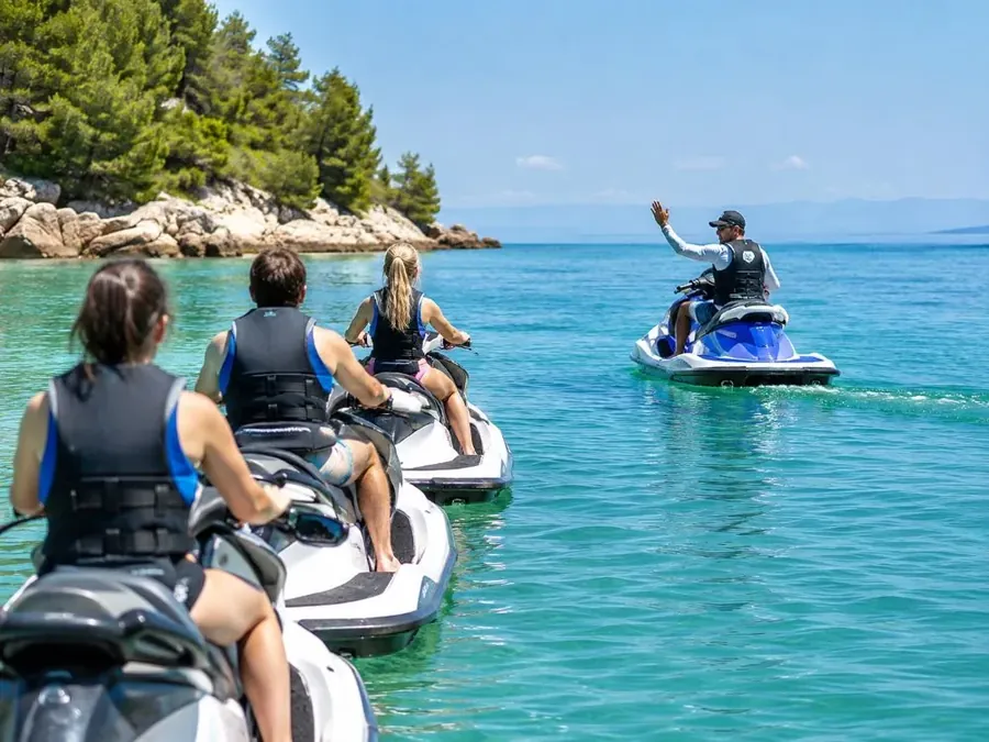 A guide raising a hand to stop a line of jet skis on the water