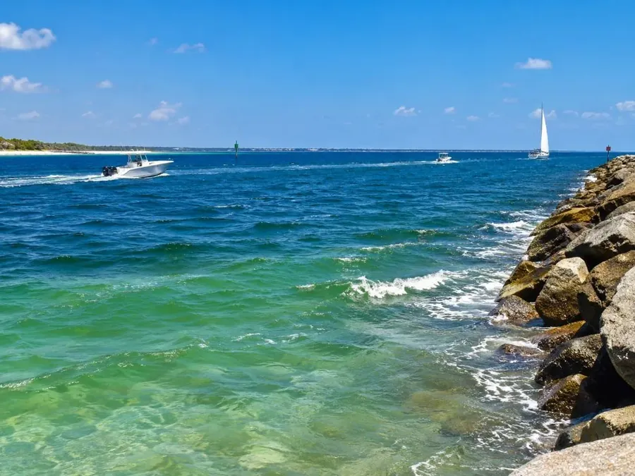 A choppy inlet where calm bay water meets open water beside a jetty