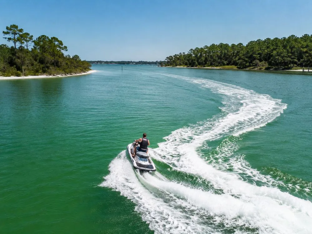 A jet ski leaving a long curving wake across a wide calm bay with low wooded shores