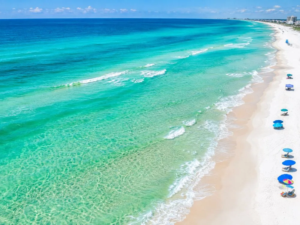Aerial view of a white-sand beach and bands of emerald and turquoise water