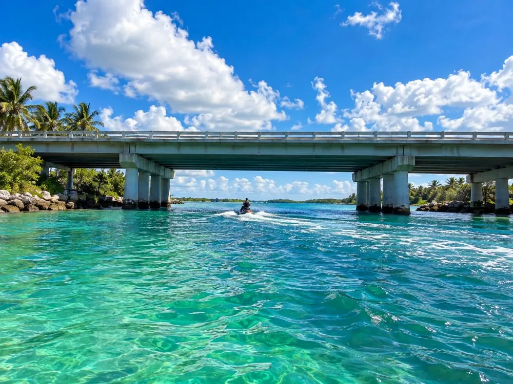 A long low concrete bridge over a green tidal pass with a jet ski far away beneath it