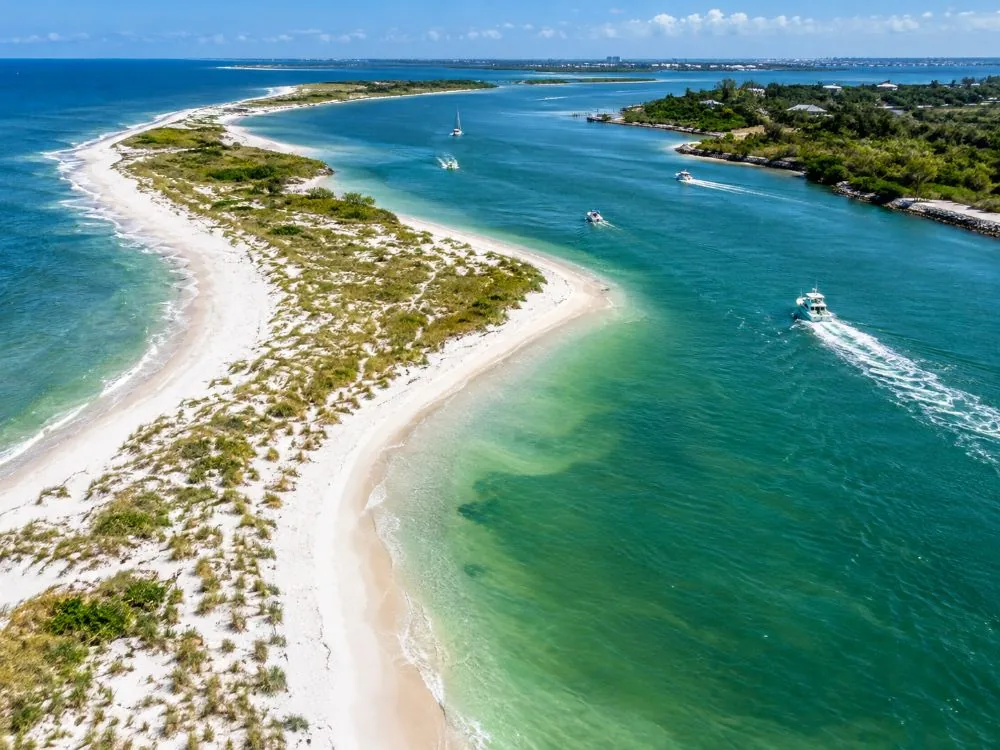 A white sand point with sea oats curving into a green tidal pass