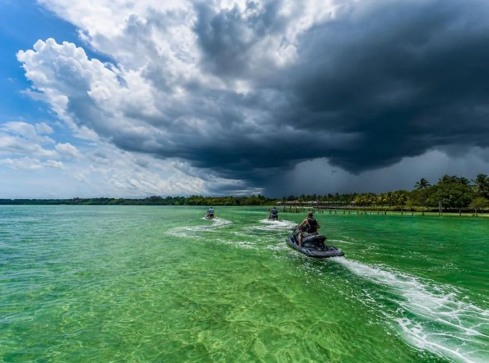 Dark thunderstorm clouds building over a sunlit bay while jet skis head back to a dock